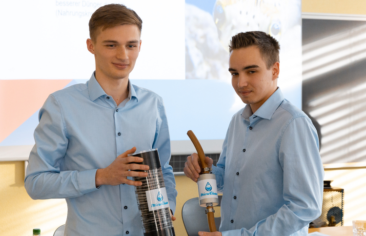 Zwei junge Männer zeigen ihr selbst entwickeltes Produkt: Einen Mikroplastik-Filter.