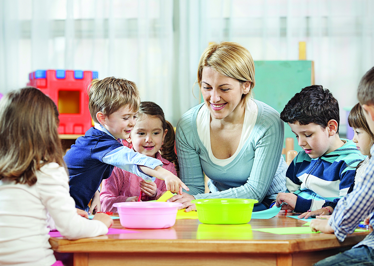 Kinderbetreuerin mit Kindern an Tisch sitzend