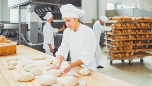 Eine Mitarbeitende in der Bäckerei knetet einen Brotteig