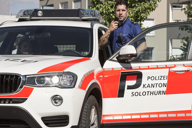 stehender Polizist funkt neben Patrouillenfahrzeug