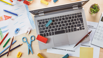 Ein Tisch, auf dem ein Laptop, Arbeitsdokumente, sowie Kinderspielsachen liegen.