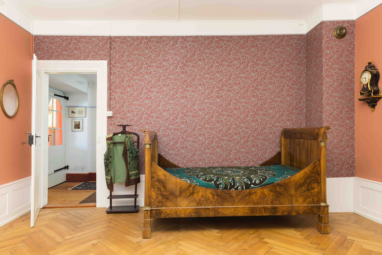 Balsthal Biedermeiervilla Ein Raum der Biedermeiervilla mit einem Bett und einer farbrigen Tapete.