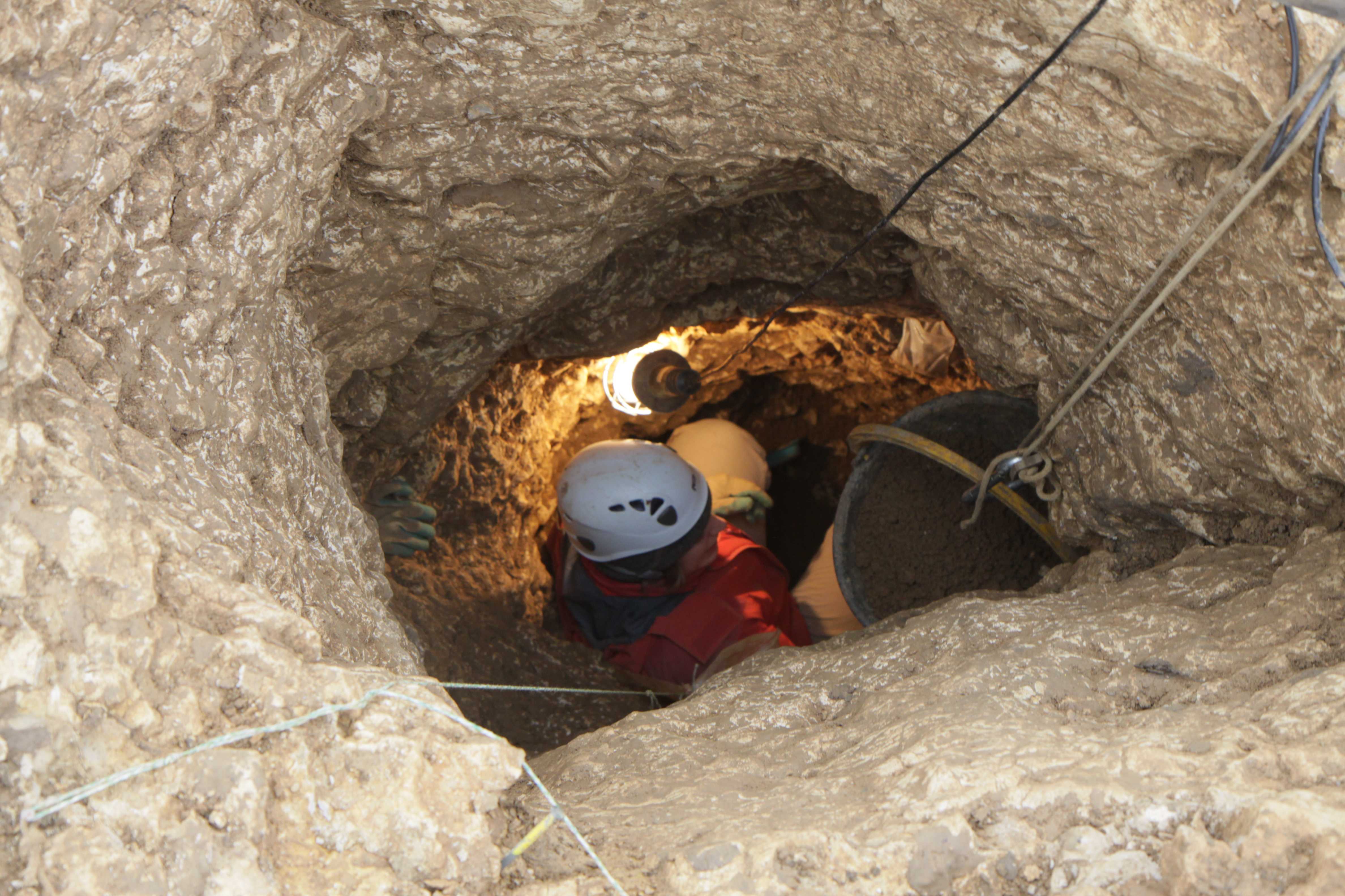 Schacht im Felsen, unten Arbeiter mit Helm