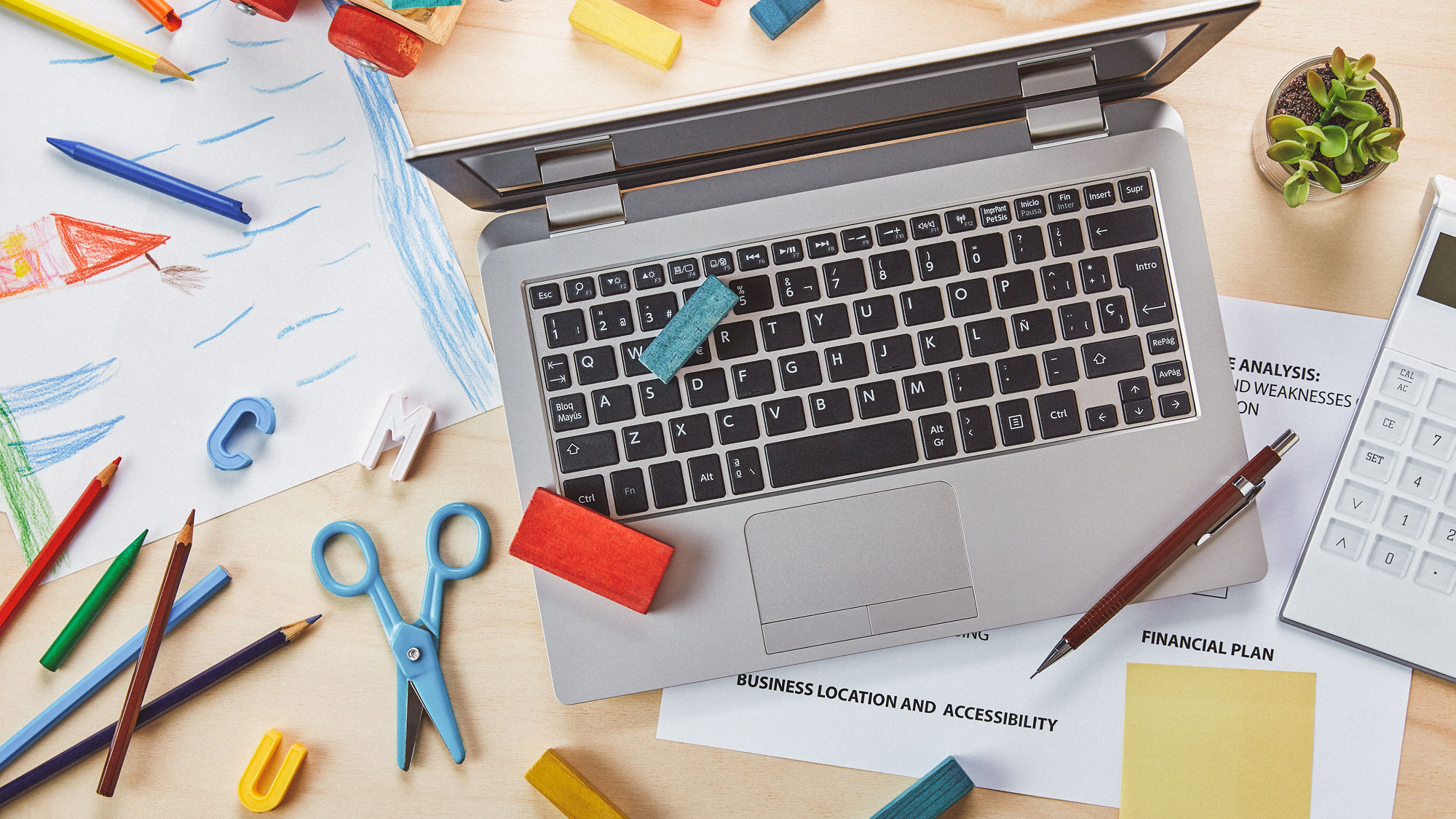 Ein Tisch, auf dem ein Laptop, Arbeitsdokumente, sowie Kinderspielsachen liegen.