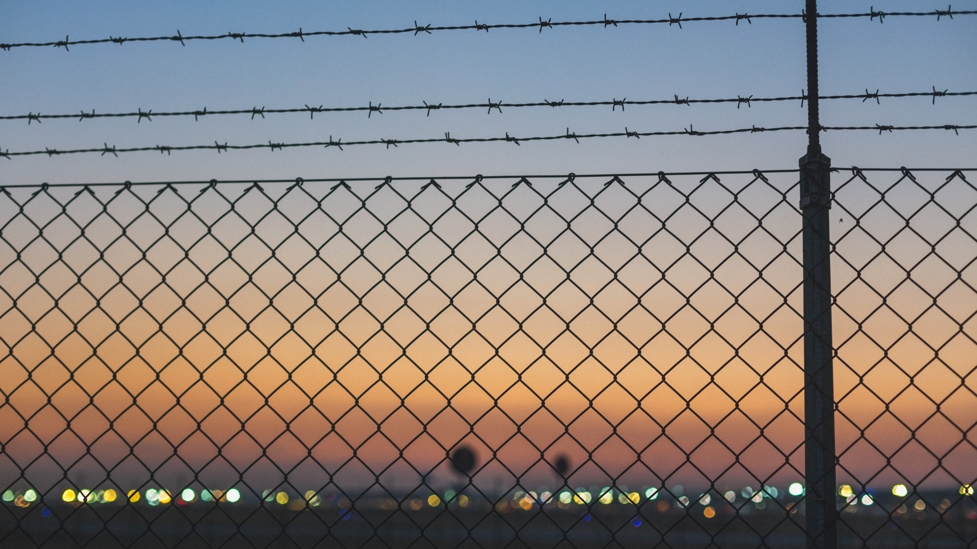 Blick durch Zaun zu Flughafengelände bei Abenddämmerung