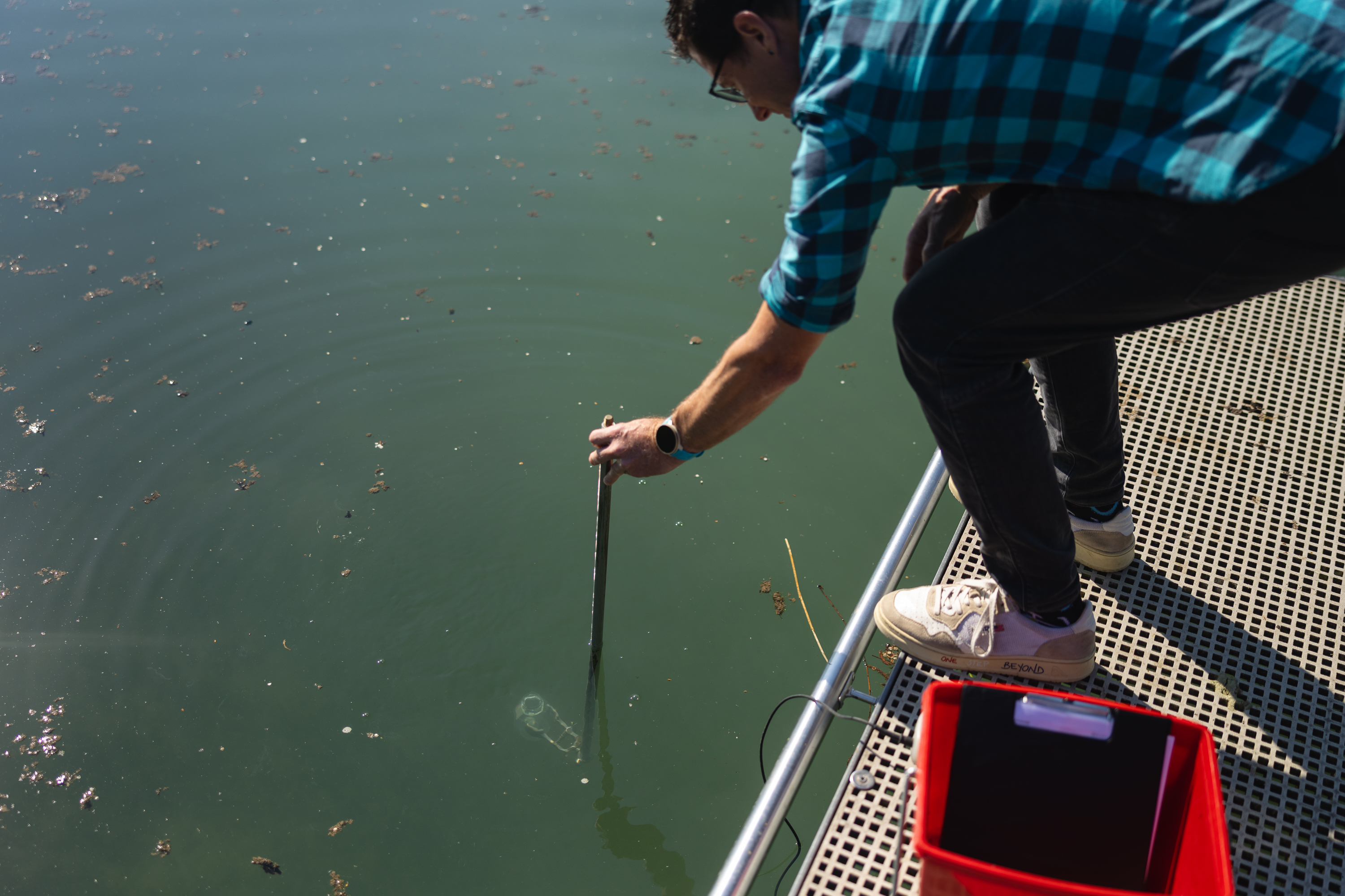Simon Stüdeli entnimmt mit Messstab eine Wasserprobe vom Steg.