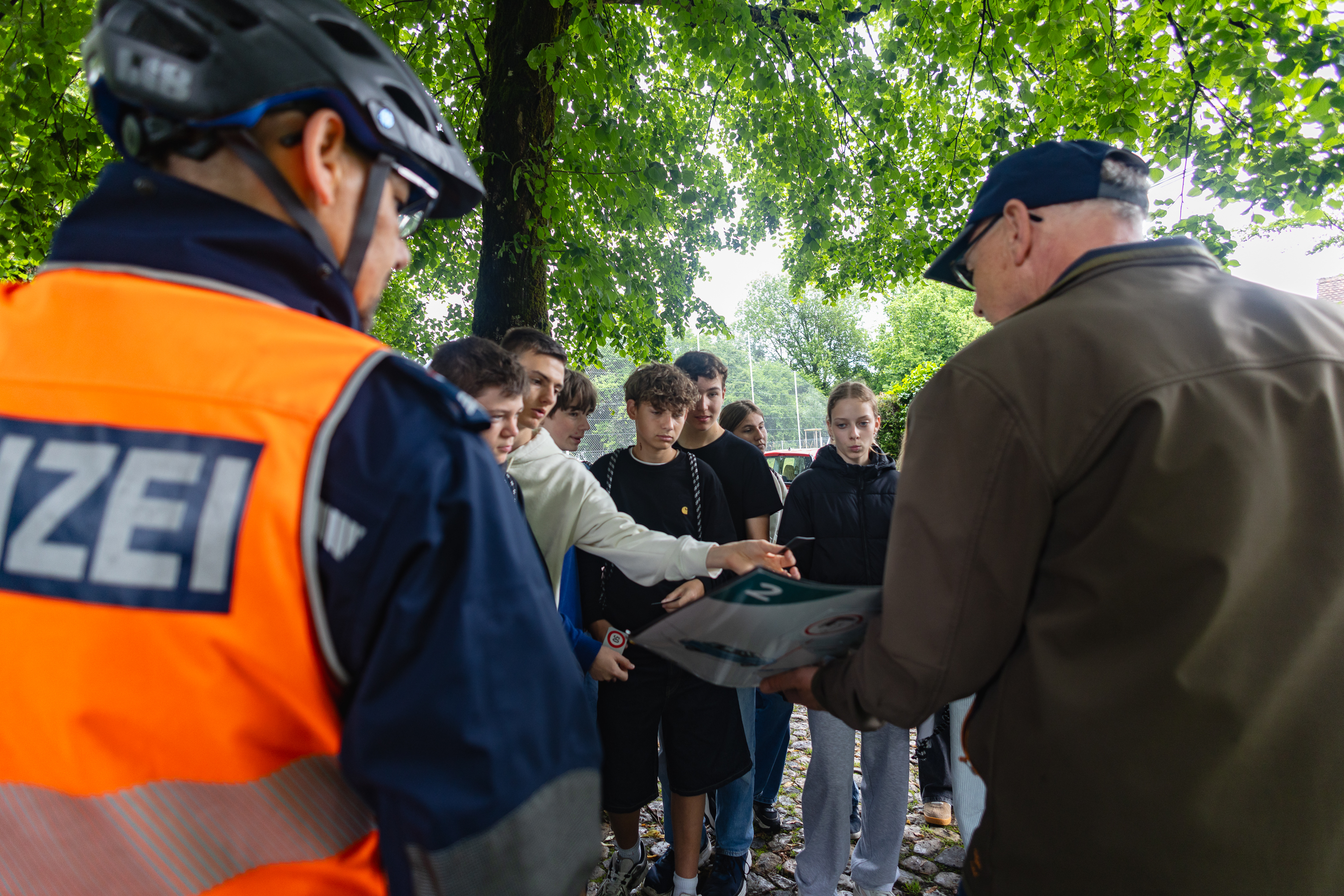 Jugendliche betrachten gemeinsam mit Polizei und Fachperson ein Plakat.