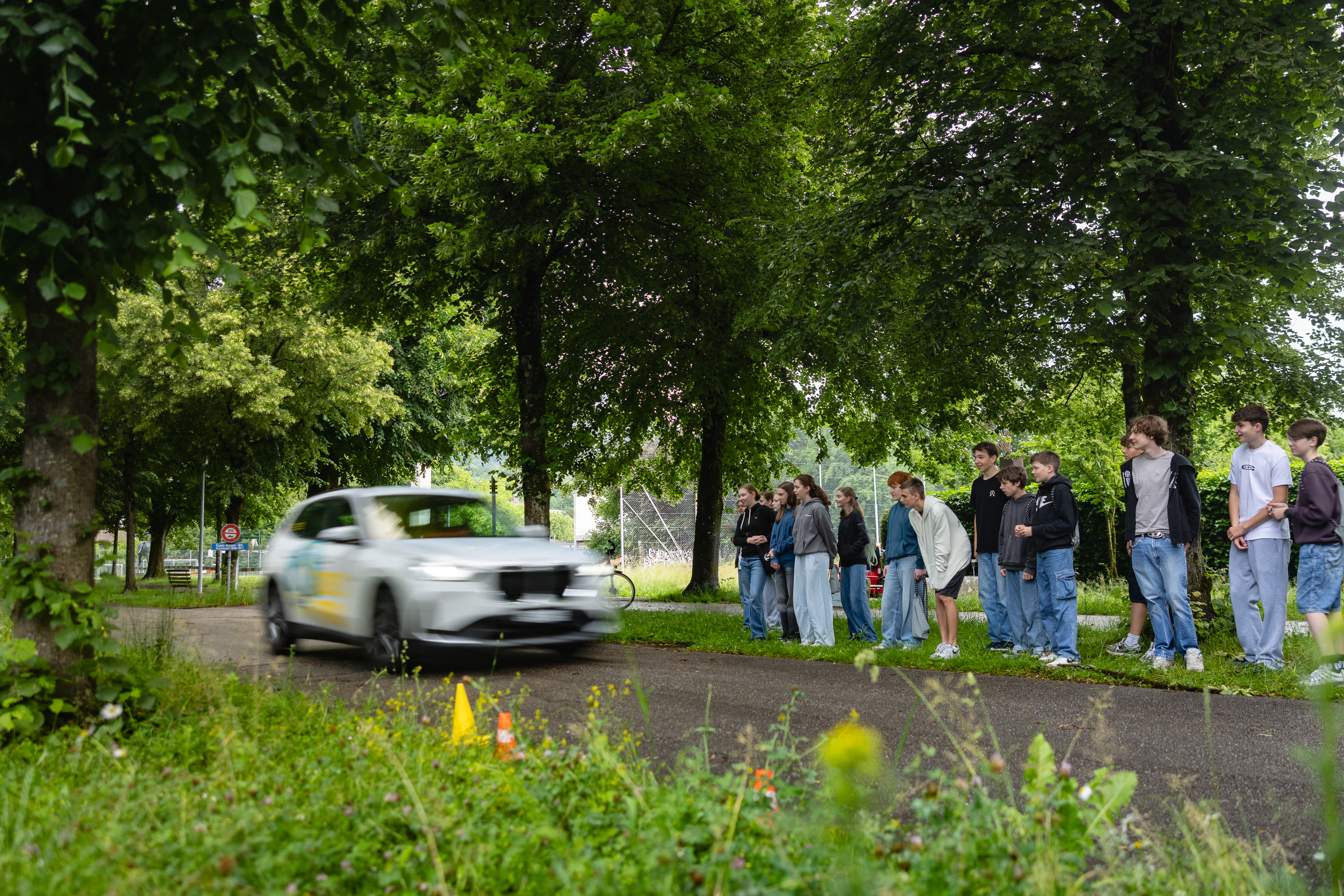 Jugendliche beobachten Bremsweg-Demonstration mit fahrendem Auto.