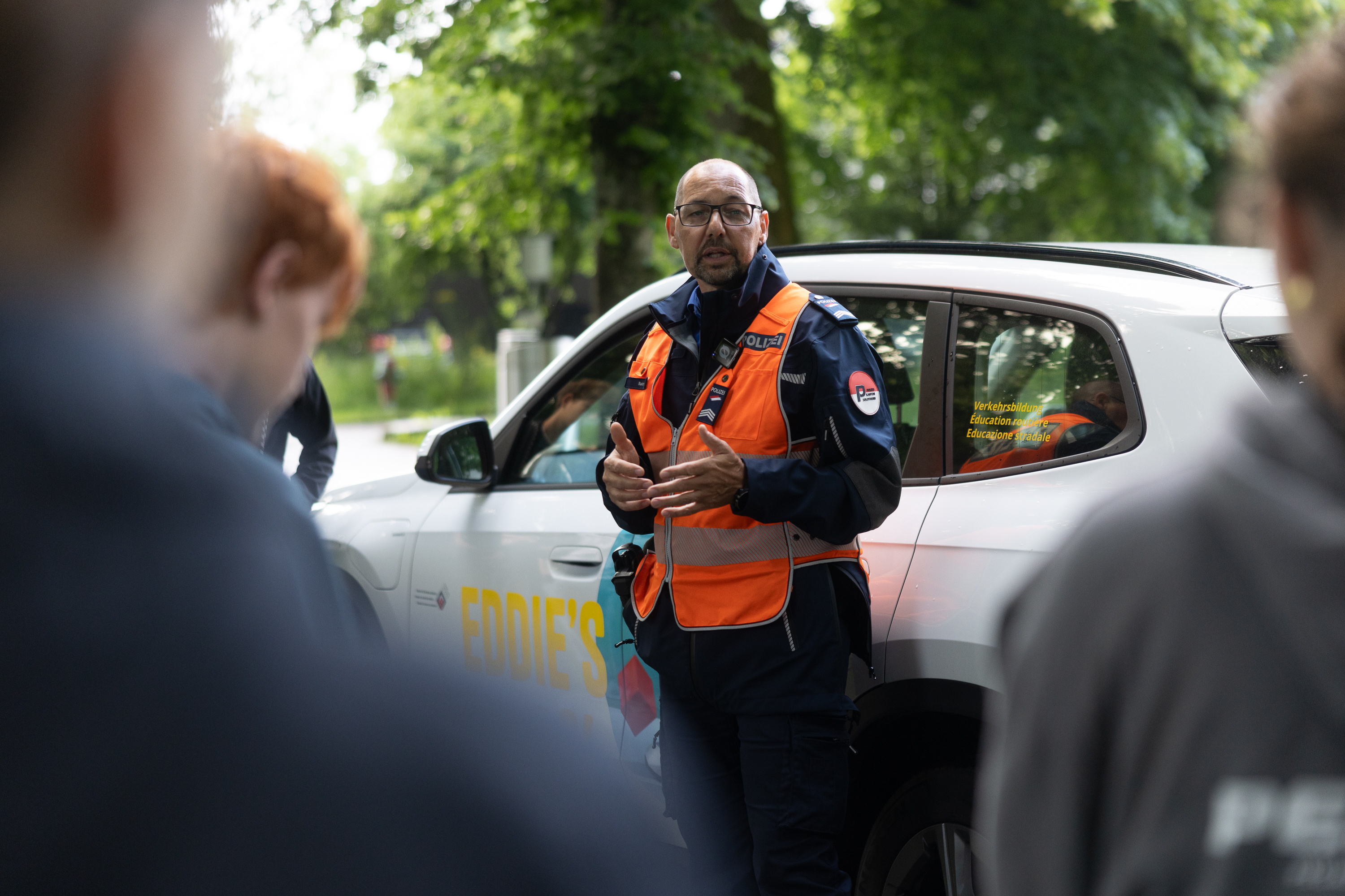 Polizist informiert Jugendliche zur Verkehrssicherheit vor Einsatzfahrzeug.