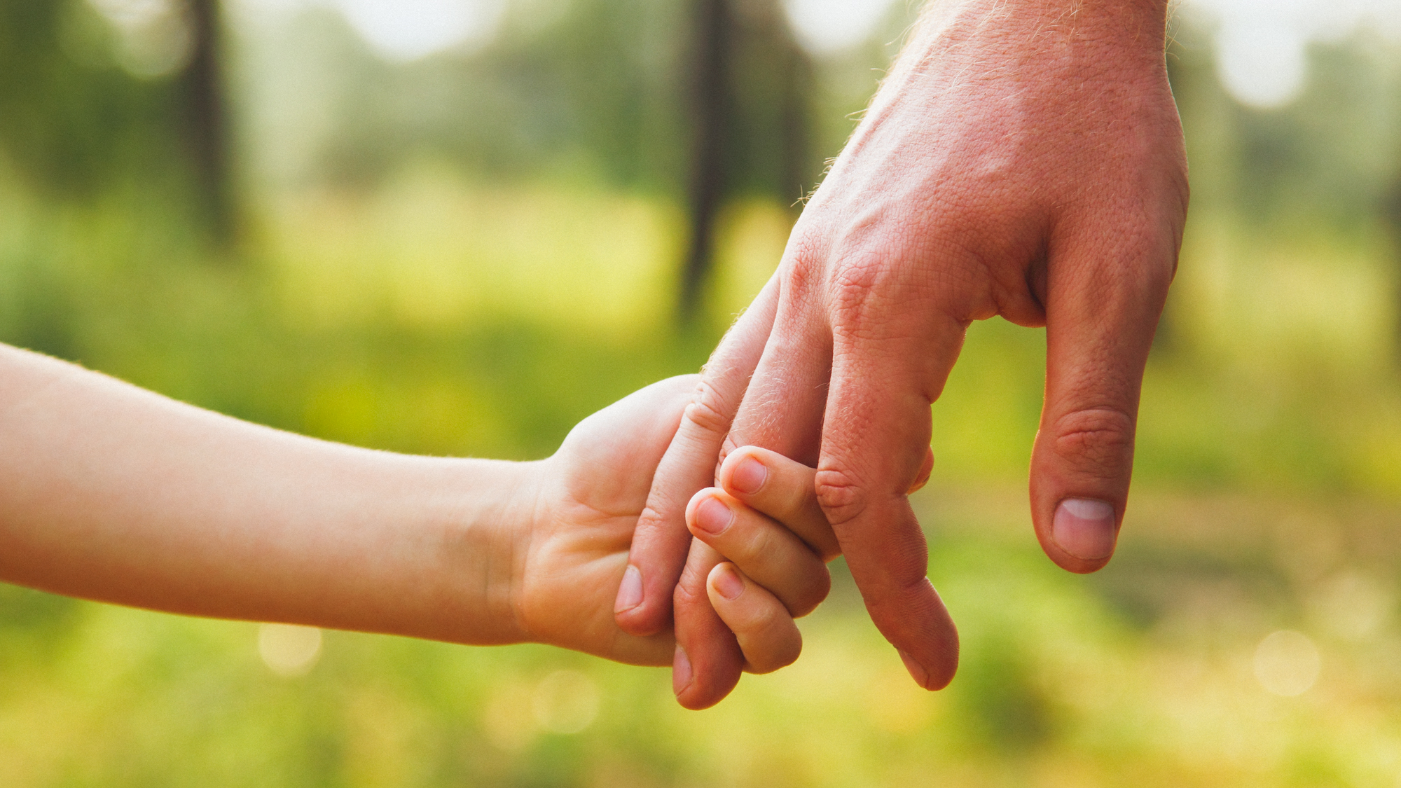 Die Hand eines Elternteils hält die Hand eines Kindes.