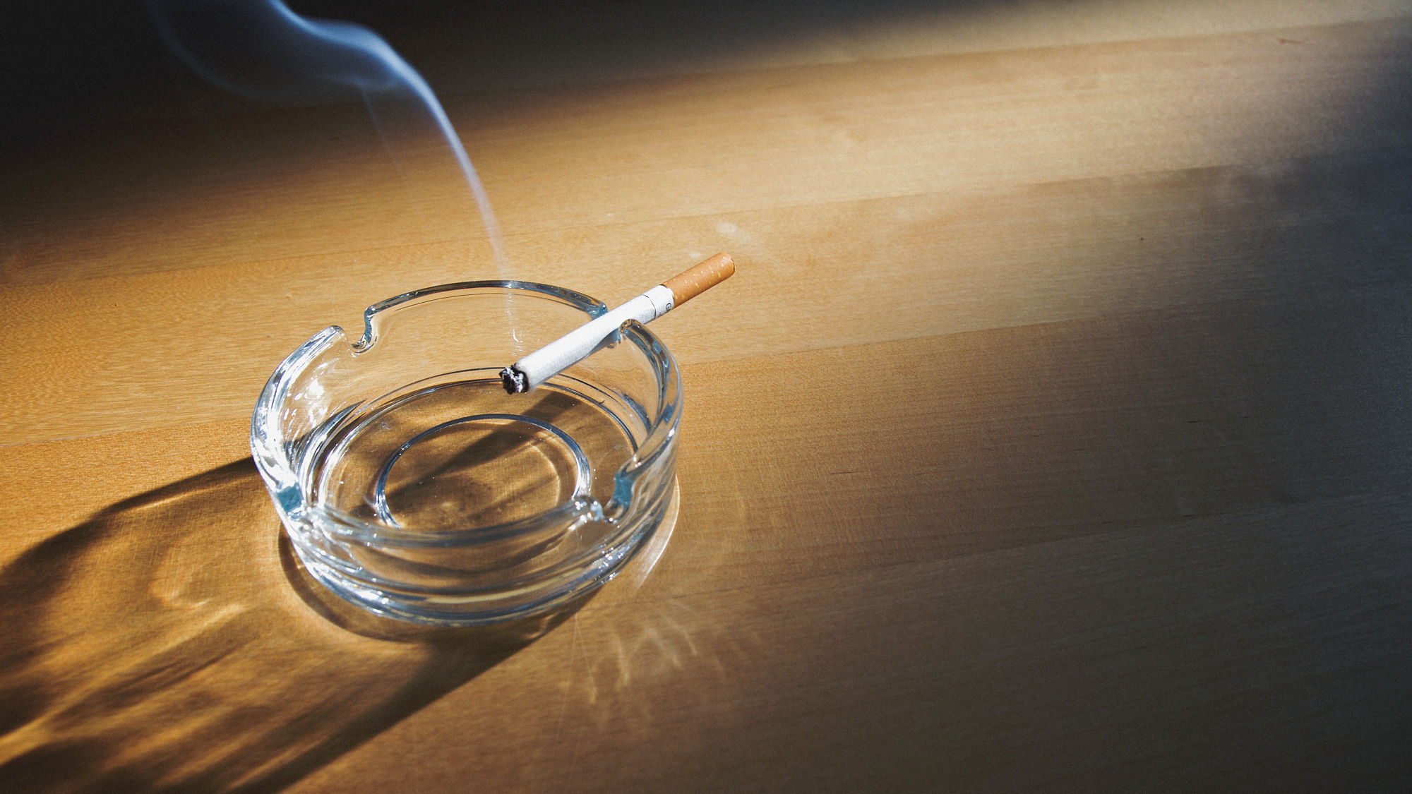 Eine brennende Zigarette klemmt in einem Aschenbecher