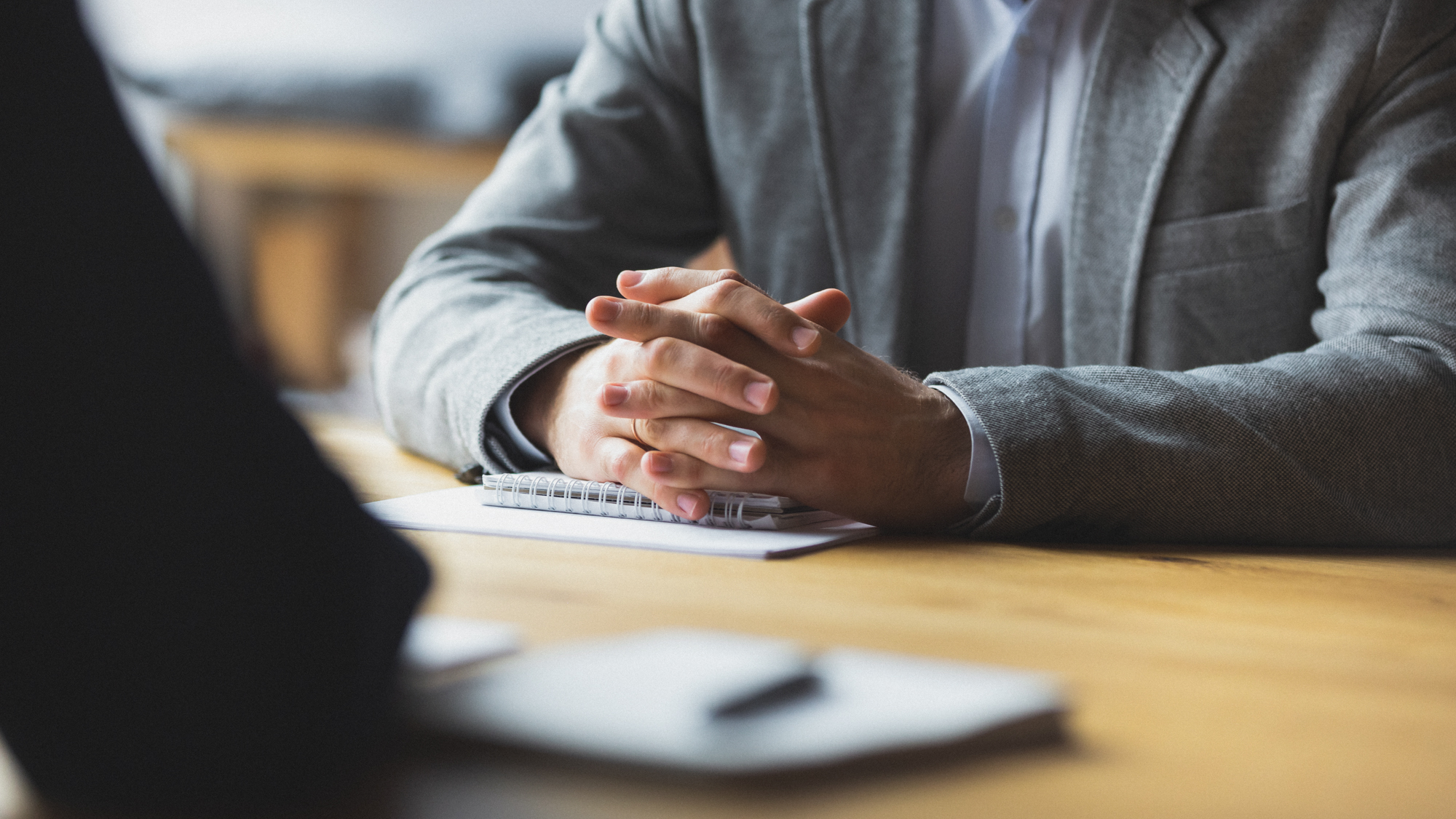 verschränkte Hände ruhen auf einem Schreibblock, der auf einem Besprechungstisch liegt