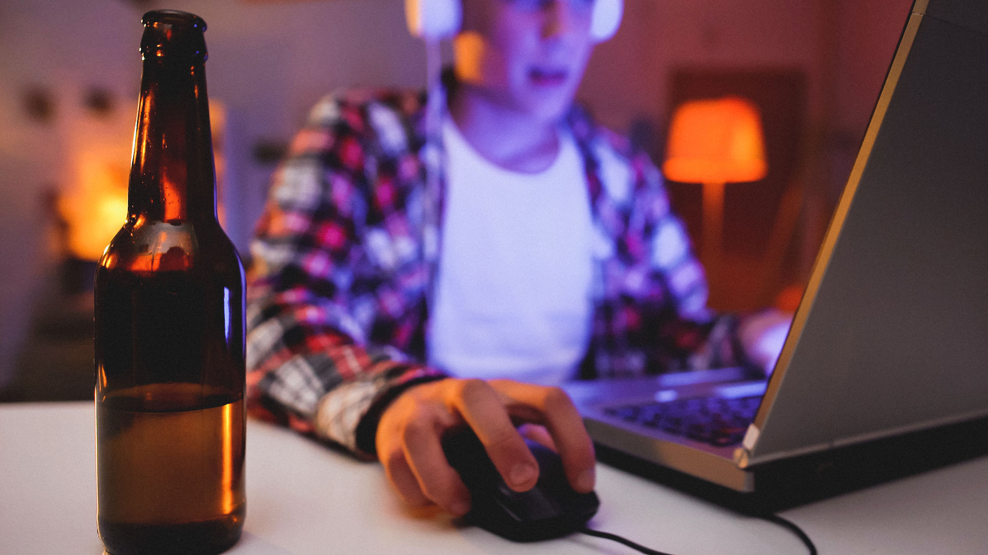 Junger Mann nachts am Computer mit Bierflasche