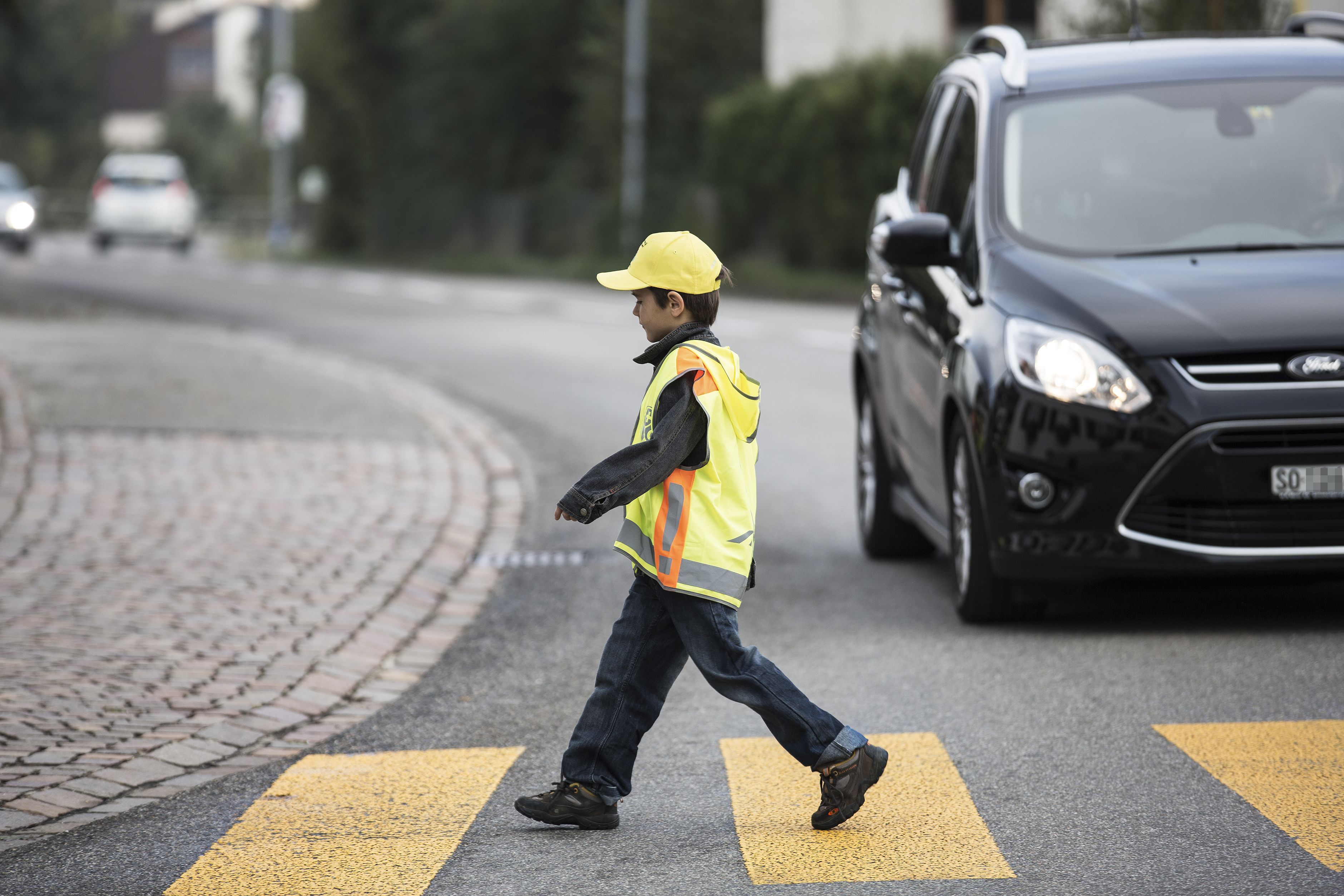 Kind läuft über Fussgängerstreifen, vor einem wartenden Auto.