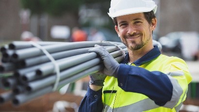 Mann auf der Baustelle mit Helm und Warnweste trägt Stahlrohre