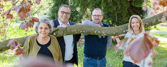 Vier Personen, die sich um einen langen horizontalen Baumast gruppieren.