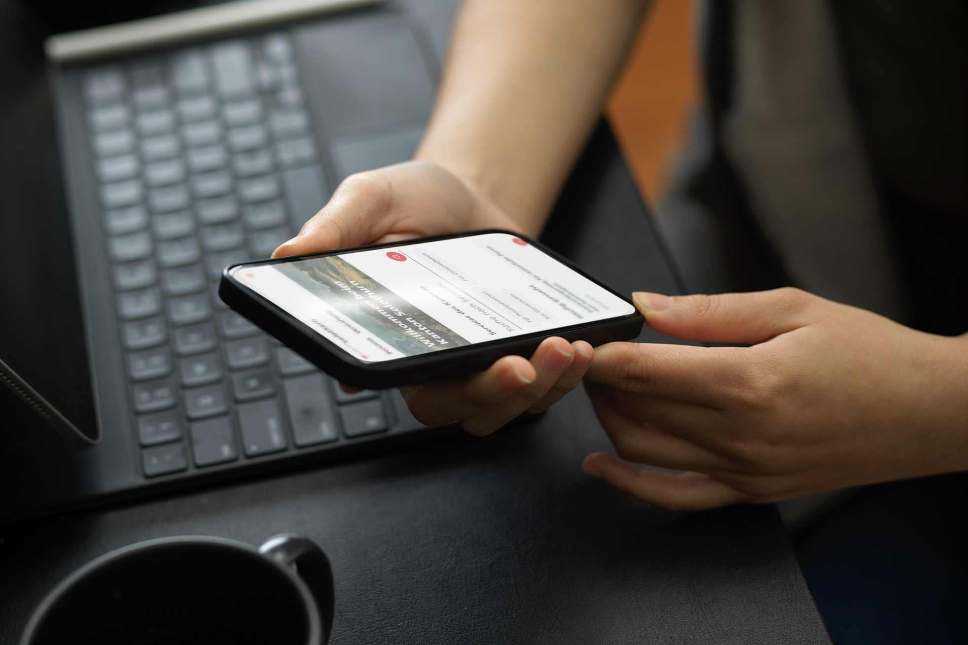 Themenbild: Person hält Smartphone in den Händen, im Hintergrund sieht man eine Tastatur