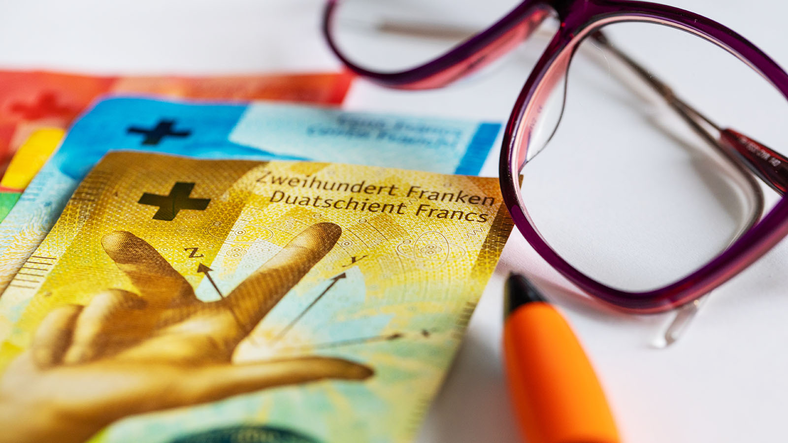 Schweizer Banknoten auf einem Tisch, daneben eine Brille und ein Stift