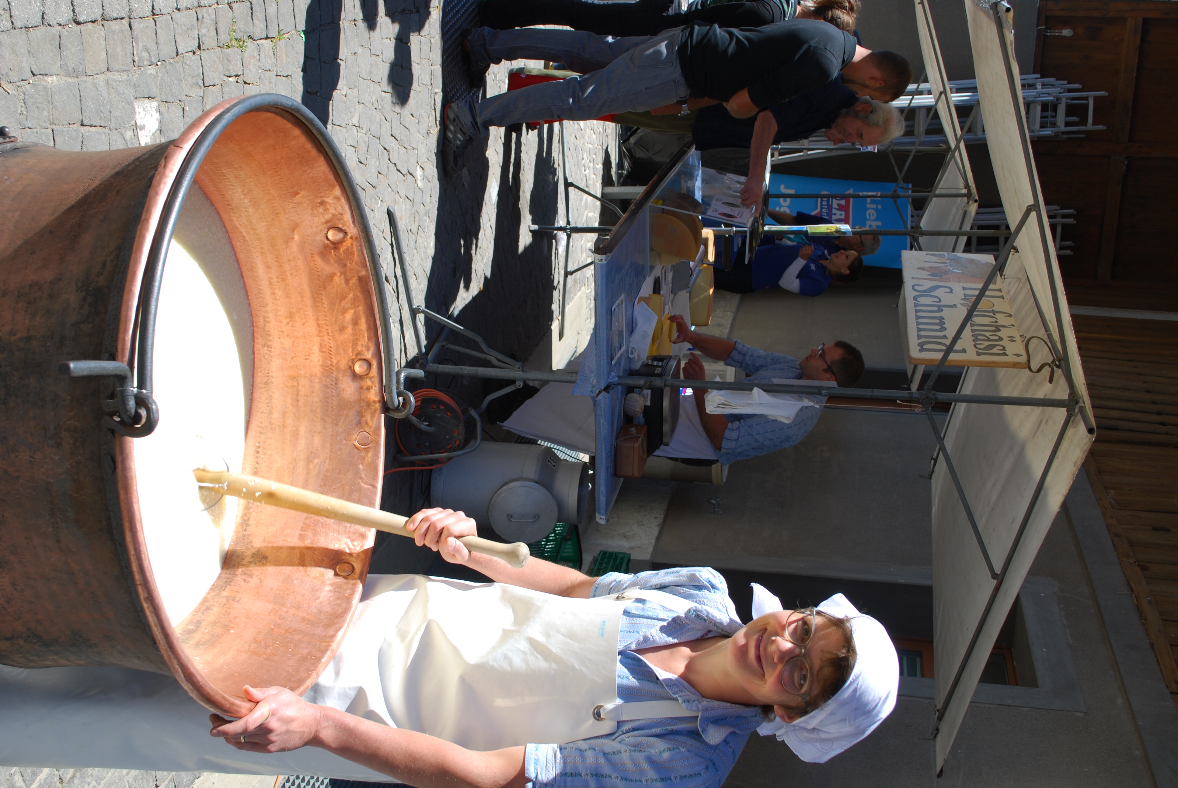 Frau auf Markt rührt mit Kelle in Topf bei Käseherstellung