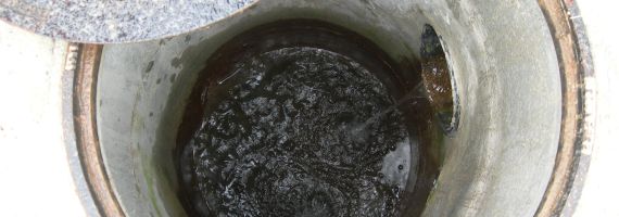Schacht Ein offener Schacht mit Schachtdeckel in den über eine Rohrleistung Abwasser läuft.